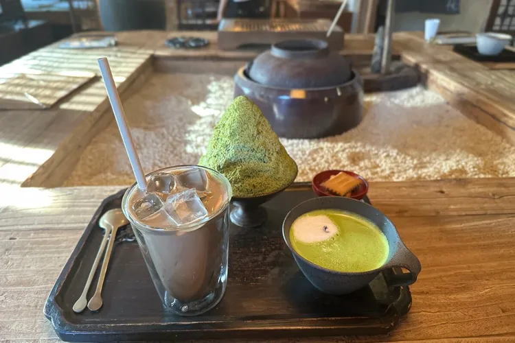 T. Nomad — matcha latte, black sesame hojicha latte, and matcha dessert on a rustic wooden tray